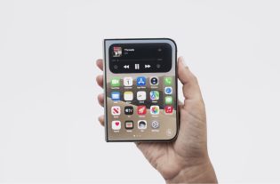 Uma mão segura um smartphone dobrável fechado, exibindo a tela externa com ícones de aplicativos e um widget de mídia no topo, contra um fundo branco neutro.