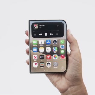 Uma mão segura um smartphone dobrável fechado, exibindo a tela externa com ícones de aplicativos e um widget de mídia no topo, contra um fundo branco neutro.